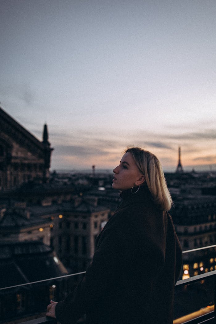 A woman gazes over Paris at twilight, with the Eiffel Tower visible. Captivating cityscape view.