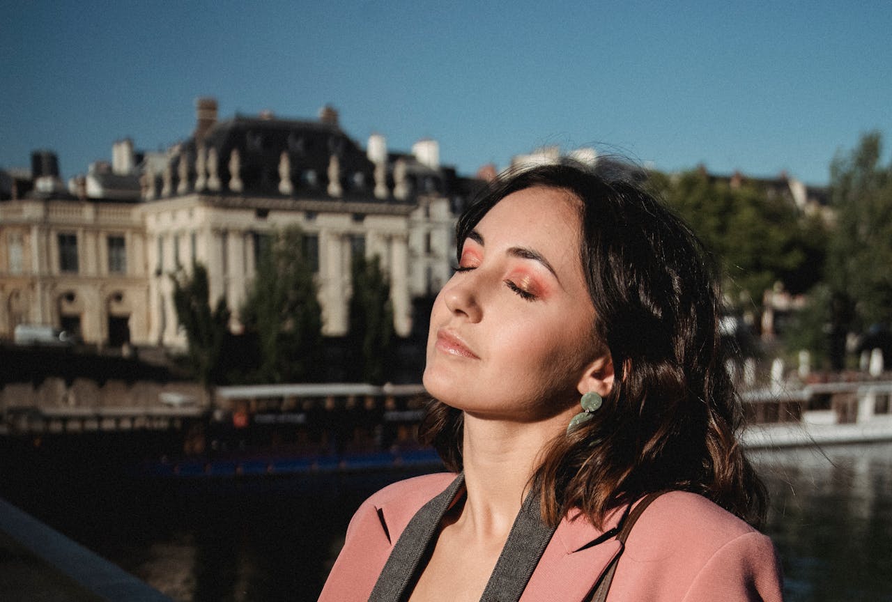Elegant woman enjoying the sunlight outdoors, with a serene expression and a historic city background.